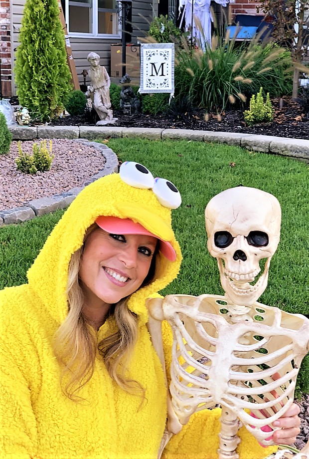 Heather Killebrew in a yellow onesie costume posing with a plastic skeleton decoration during a Halloween party in Wentzville, MO